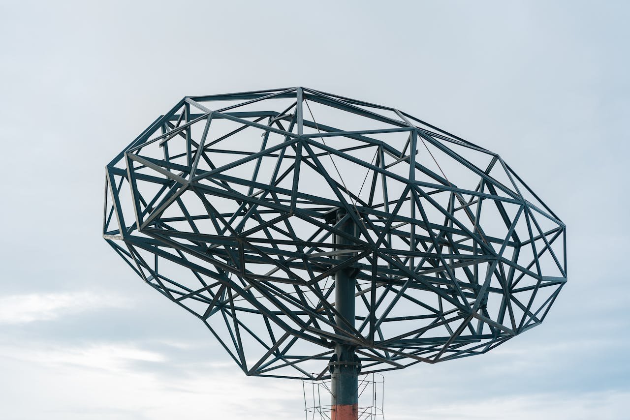 Artistic steel sculpture with geometric design standing prominently against a cloudy sky.